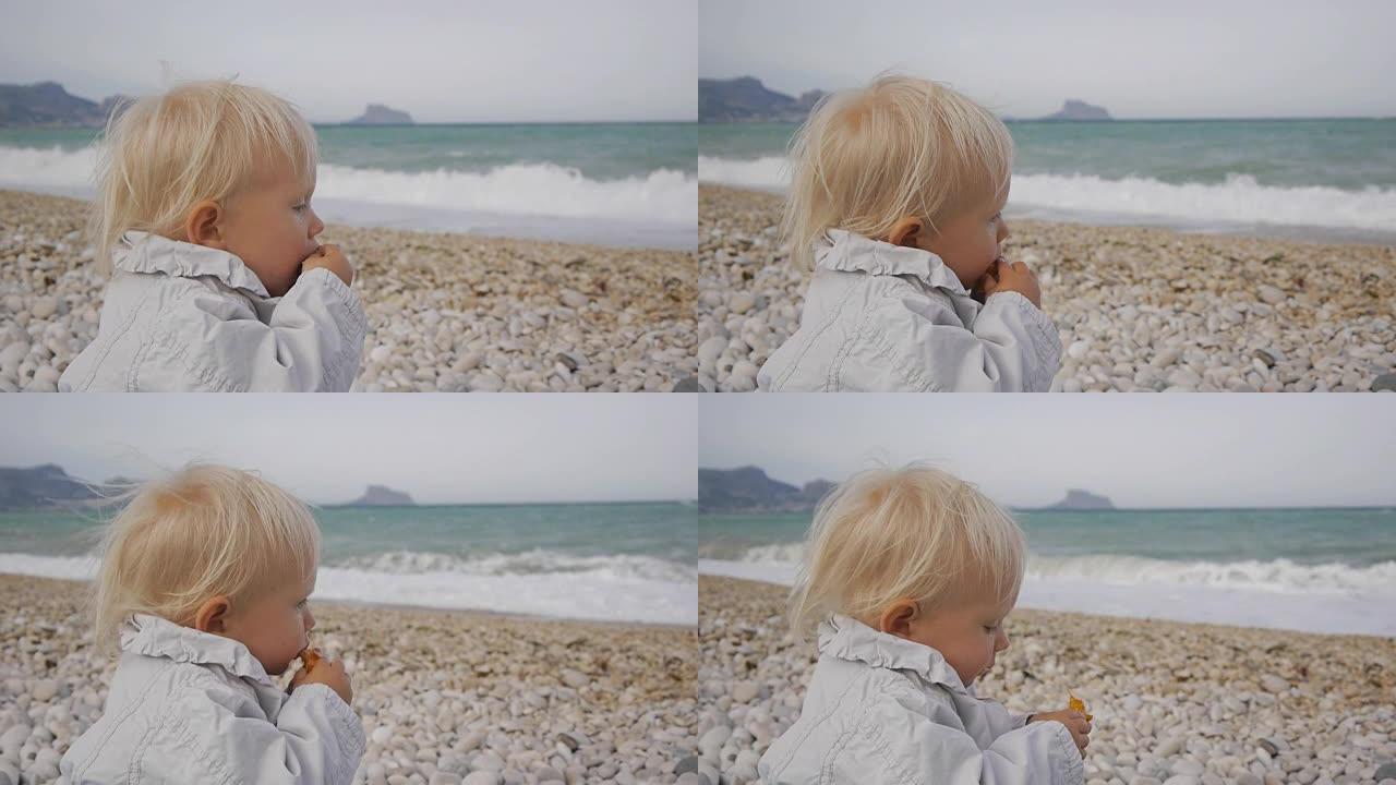 在暴风雨的海浪背景下，白种人金发碧眼的女婴在吃枸杞的果实时含泪。