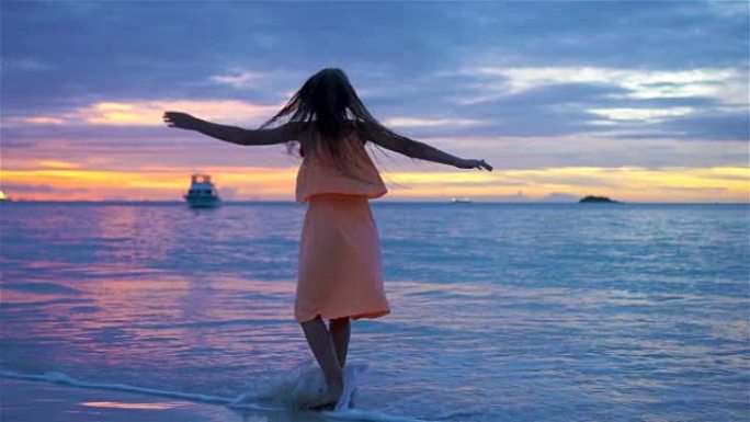 日落时在海滩上跳舞的小女孩的Sihouette。