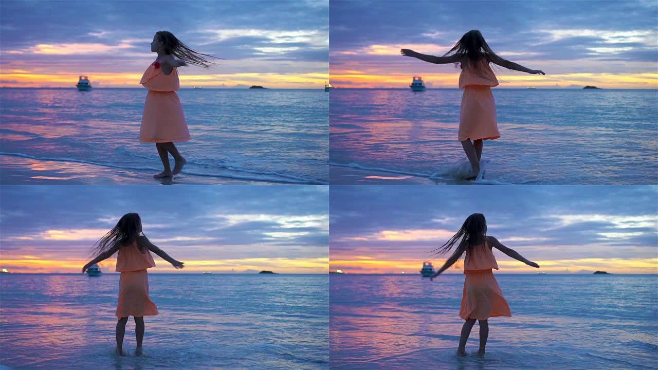 日落时在海滩上跳舞的小女孩的Sihouette。