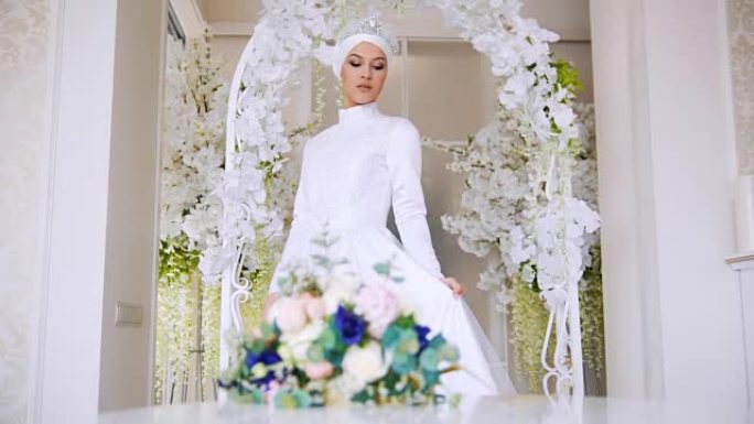 美丽的新娘穿着白色传统穆斯林礼服，配有一束鲜花