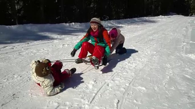 快乐的家庭在冬天在山上的白雪皑皑的森林里玩耍。妈妈和她的两个孩子在拉雪橇。他们在笑。