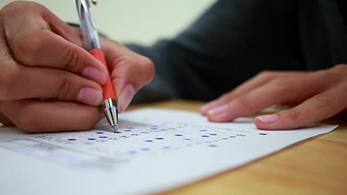 学生手拿考试，用铅笔在标准化考试的光学形式上书写考场，并在教室里做期末考试。