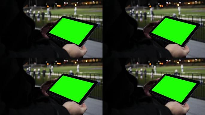 男子在看台上的足球队练习赛上观看绿屏平板电脑-特写角度