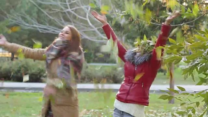两个女孩在秋天森林的背景下扔树叶，享受和乐趣