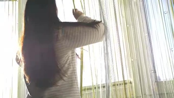 woman opening window curtains at home, back view. 