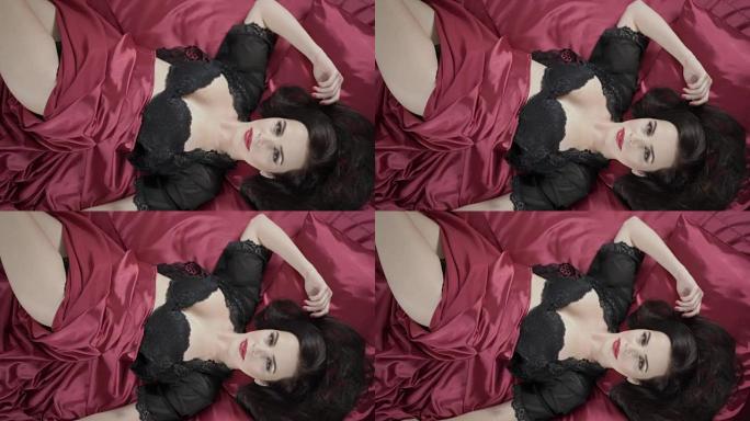 性感的女人与完美的身体躺在她的背部横跨红色的床单