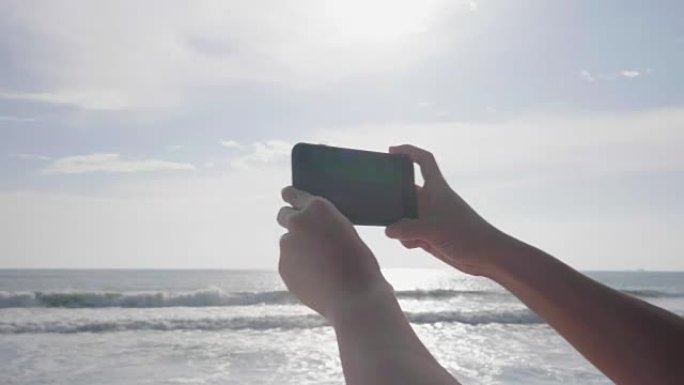 度假时，日落时在海边的海滩上用智能手机拍照。