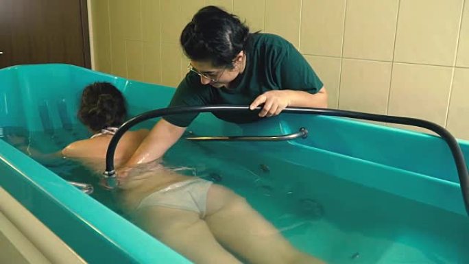 一位女性水力按摩大师用淋浴喷头按摩女孩的腰部