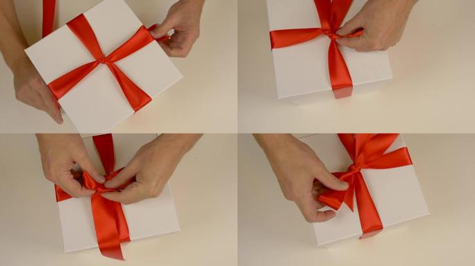 包装白色礼品盒。高加索人手包装礼品盒。男人的手在白色纸板箱上系上红丝带。俯视图特写。红色缎带丝带。