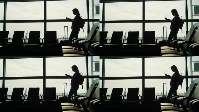 一个大窗户上的女人的剪影，喜欢平板电脑。候机楼机场，等待您的航班