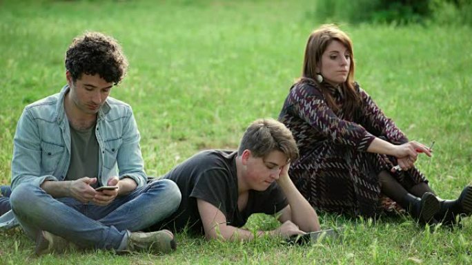 三个年轻的学生在公园里的草坪上放松聊天，大笑和放松
