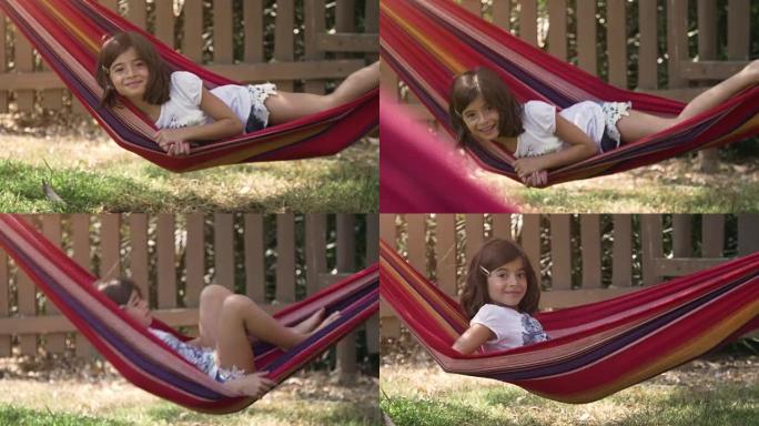 夏令营中年轻快乐的小女孩躺在五颜六色的吊床上放松在外面玩绿草地上的plushes狗娃娃儿童慢动作