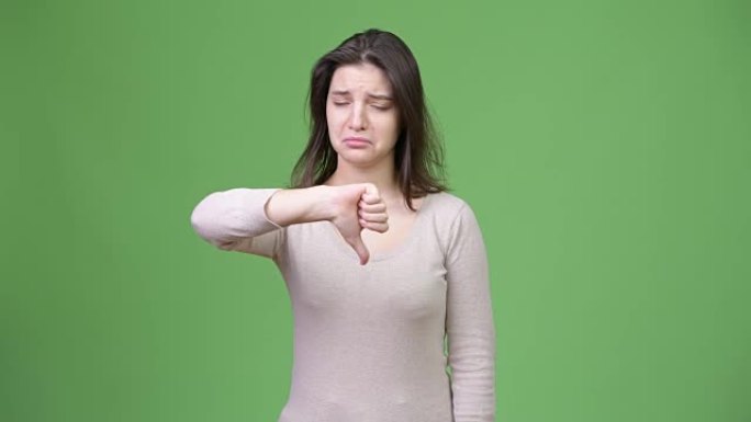 年轻悲伤的女人在绿色背景下竖起大拇指