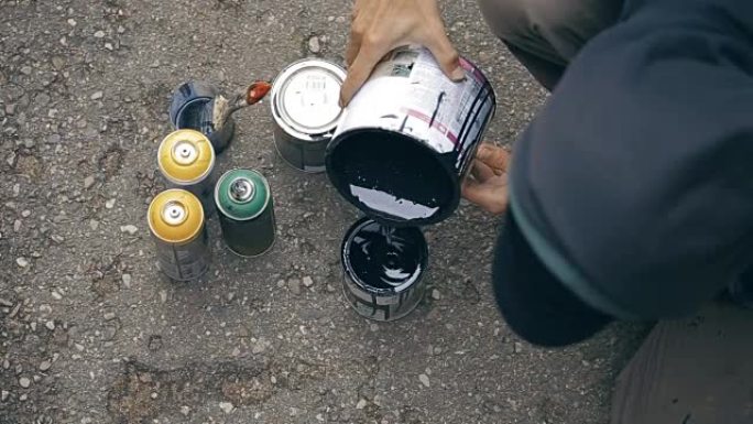 艺术家将黑色油漆搅拌到一个罐中，然后将其倒入另一个罐中。