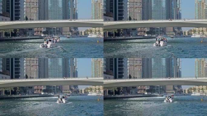 在阳光明媚的日子里，现代游艇漂浮在迪拜码头运河上，在桥下移动