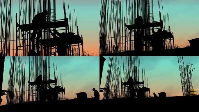 在金属框架后面，工人在日落时用电线将电线杆固定到建筑工地的钢筋混凝土支柱的底部