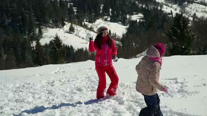 快乐的家庭在冬天在山上的白雪皑皑的森林里玩耍。妈妈和她的两个孩子扔雪球。他们在笑。