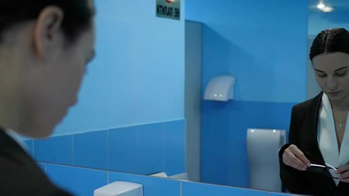 冷漠，沮丧的年轻女子在公共洗手间脱下眼镜，照镜子。
