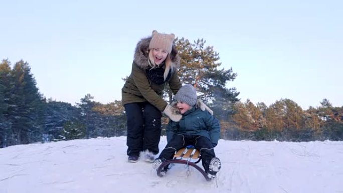 冬日，快乐的年轻女子将儿子从雪山推上雪橇，以慢动作追赶他