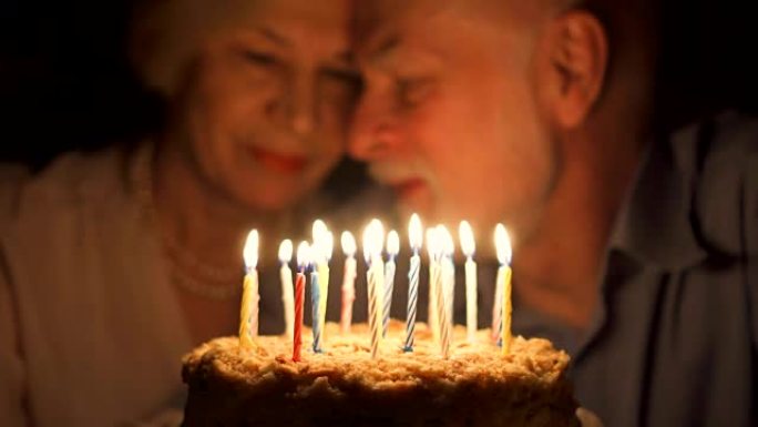 充满爱心的高级夫妇晚上在家用蛋糕庆祝周年纪念日。吹灭蜡烛