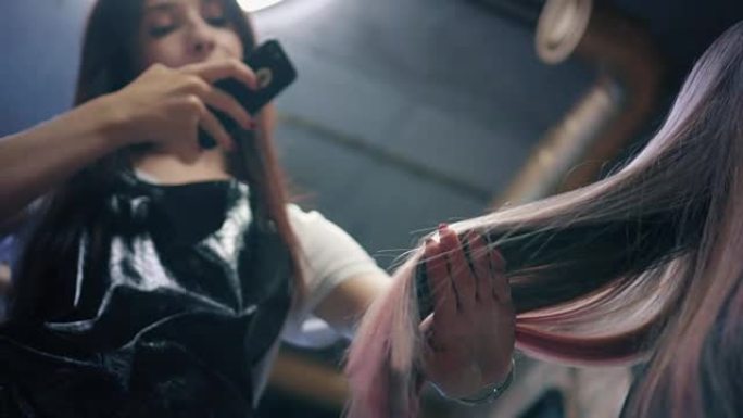 美发师在美发沙龙的智能手机上拍摄女性长发的照片。美发师钦佩她的工作，并展示了一束染发。向下角度。慢m