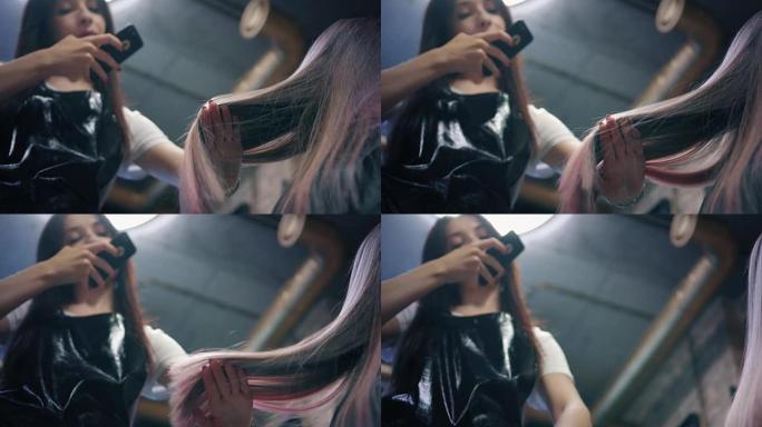 美发师在美发沙龙的智能手机上拍摄女性长发的照片。美发师钦佩她的工作，并展示了一束染发。向下角度。慢m