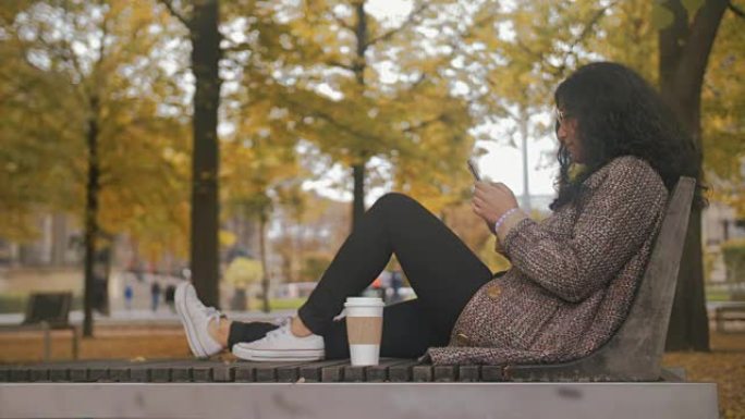 在秋季公园的长凳上的多种族女孩触摸智能手机屏幕并写下聊天消息女性的想法和梦想