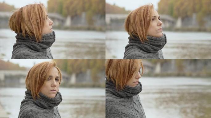 在寒冷的冬日里，一个悲伤的沉思女人站在河边的肖像