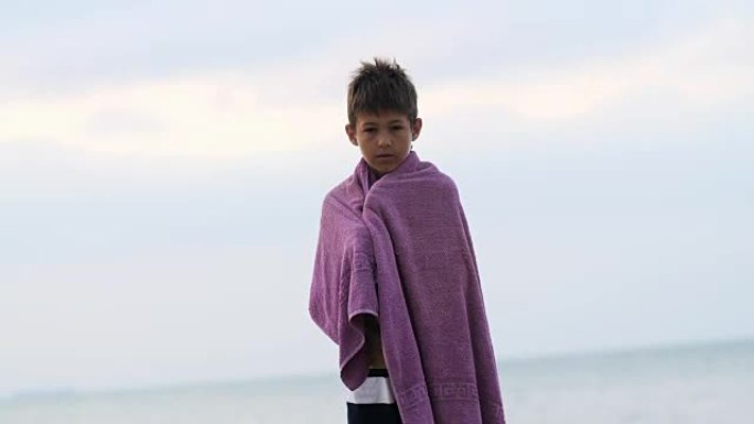 穿着毛巾的疲惫悲伤的难民男孩独自站着看着镜头，男孩正在努力保暖