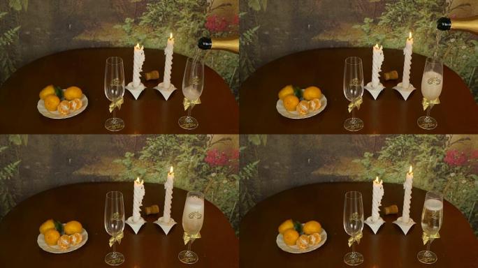 将起泡的香槟葡萄酒倒入木制背景下的玻璃杯中。桌上盘子里的普通话。成对蜡烛发出的光。晚上在室内拍摄。