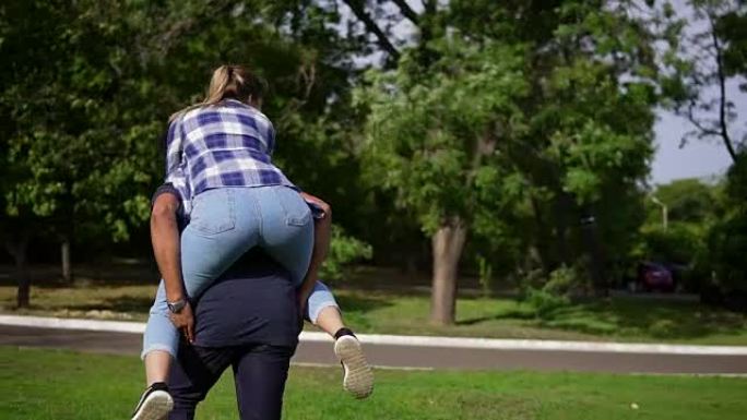 英俊的非洲小伙子piggy着他的高加索人快乐的女友，在阳光明媚的公园里的绿草地上跑来跑去。幸福的多民