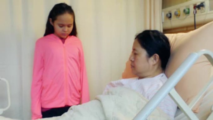 女儿站在生病的母亲的床上，躺在医院的病床架子上。