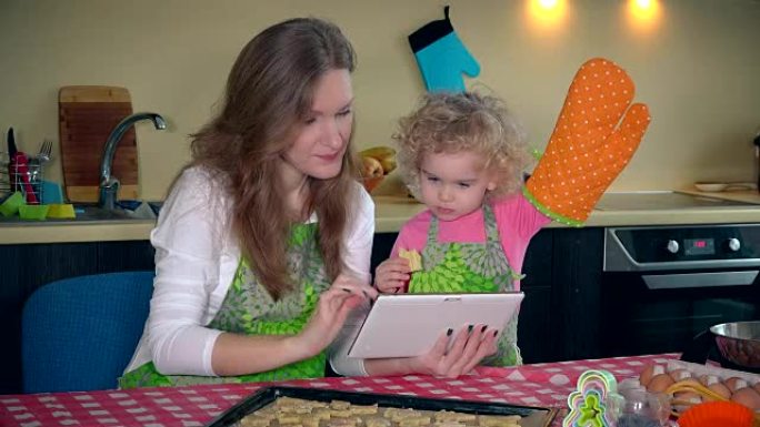 妈妈带着可爱的小女儿女孩在平板电脑上学习饼干食谱
