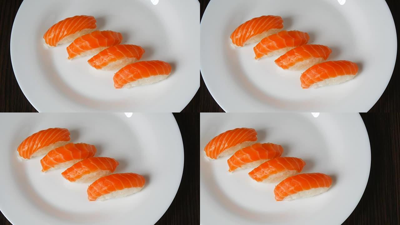 在白色的大盘子上躺着四个鲑鱼。日本料理