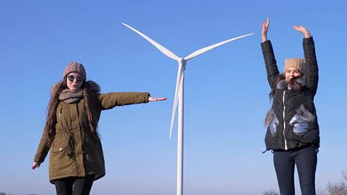 能量转换，开朗的朋友在蓝天下的风力发电机附近玩得开心