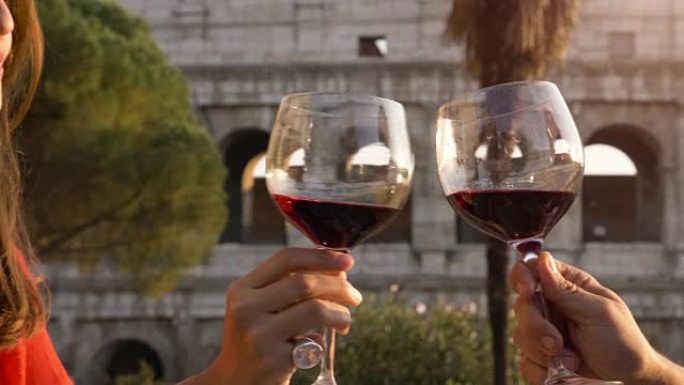 浪漫的情侣在日落时坐在罗马罗马斗兽场前的餐厅餐桌旁喝酒和敬酒