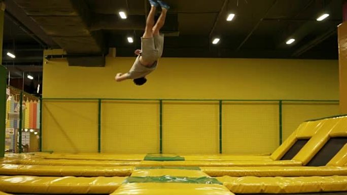 穿着米色t恤和短裤的年轻男运动员跳上蹦床，翻筋斗和身体扭曲采摘。