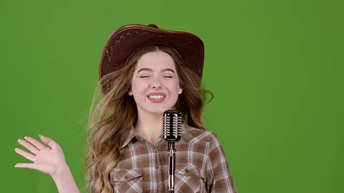 戴着皮帽的牛仔女孩对着复古麦克风唱歌。绿屏。慢动作