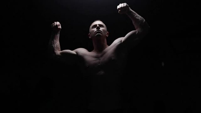 Shirtless bodybuilder posing in dark