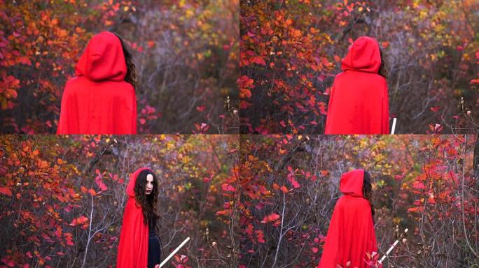 年轻漂亮的黑发女巫，穿着红色斗篷，在神秘的秋天森林里。