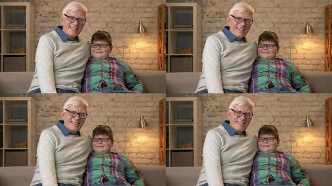 爷爷和孙子戴着眼镜，坐在沙发上，微笑着看着镜头。家庭舒适，家庭田园诗，舒适概念60 fps