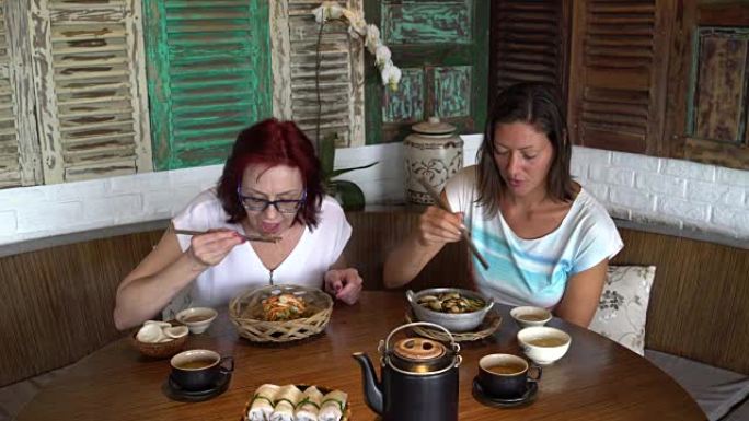 两个女人在餐馆里用筷子吃饭，聊天