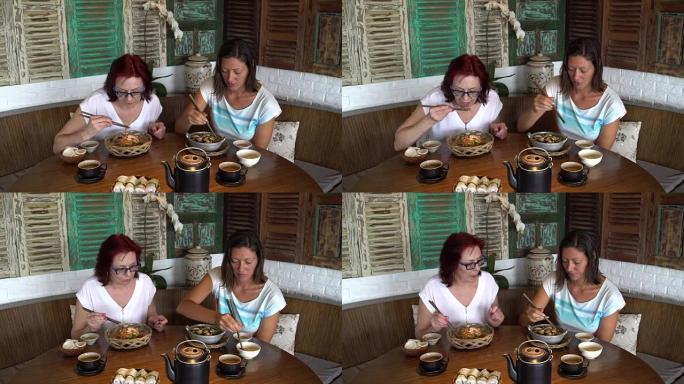 两个女人在餐馆里用筷子吃饭，聊天