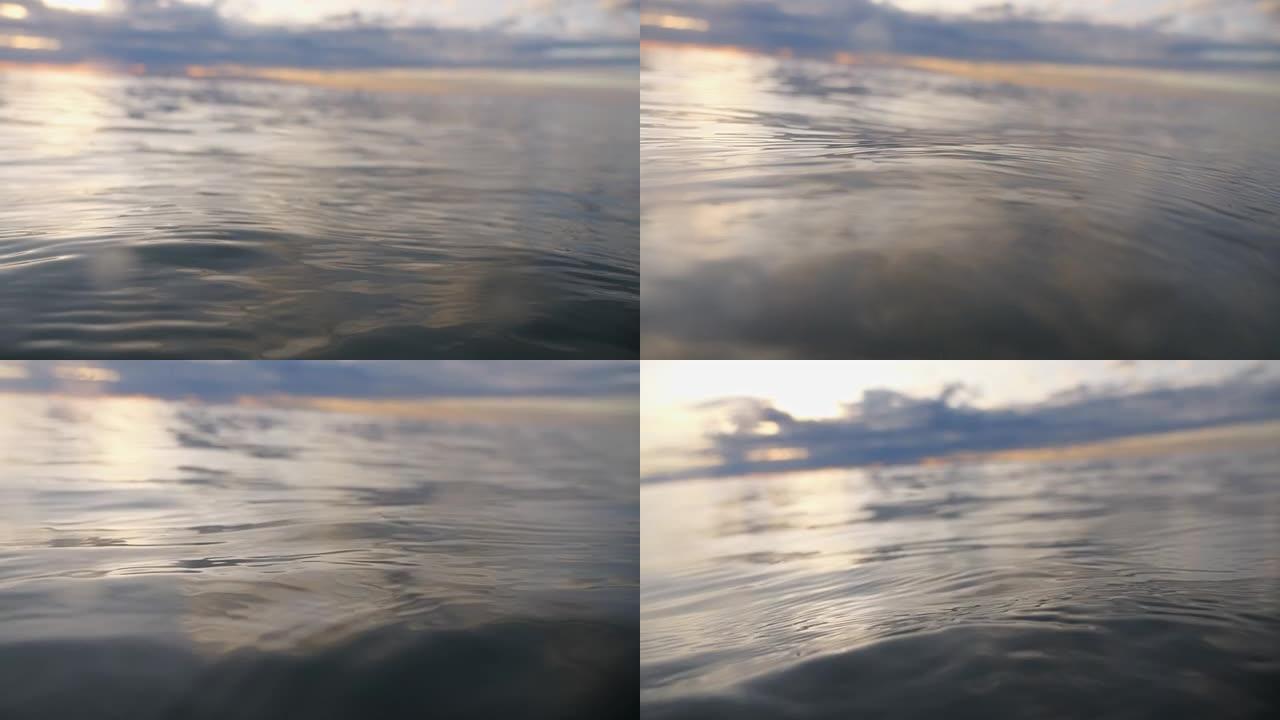 在水面上方平衡，相机沉入水下。低沉的太阳在水面上反射在波浪中。日出时潜水。