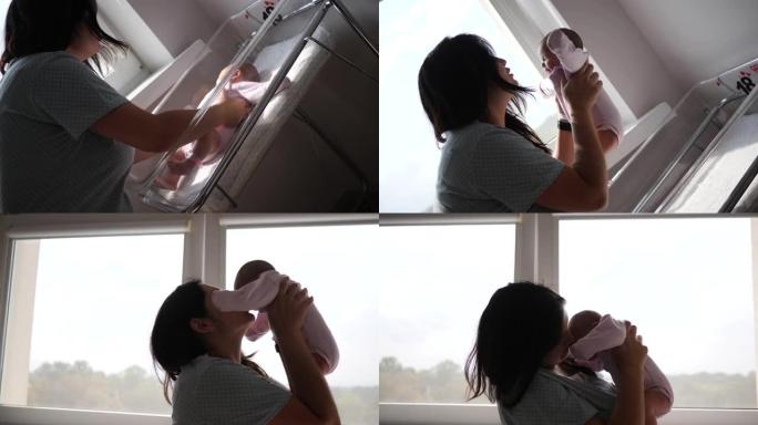 快乐的母亲将她的新生婴儿从妇产医院的病床上抱在窗户旁