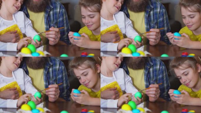 复活节家庭传统。父亲和两个白种人快乐的孩子，他们坐在家里的桌子上，用兔子耳朵染成鸡蛋，用油漆装饰鸡蛋