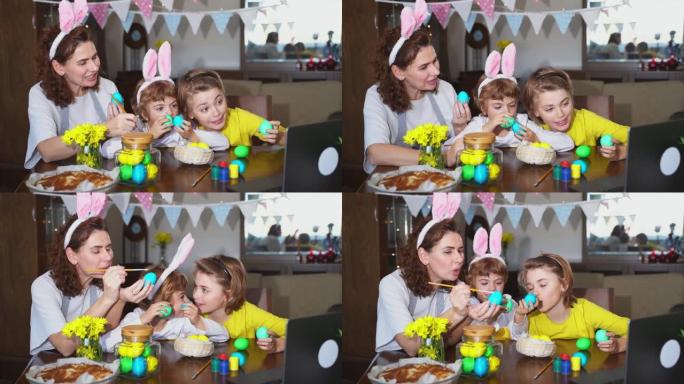 复活节家庭传统。妈妈和两个白种人快乐的孩子用兔子耳朵染成鸡蛋，并在假期用油漆装饰鸡蛋，同时坐在家里复