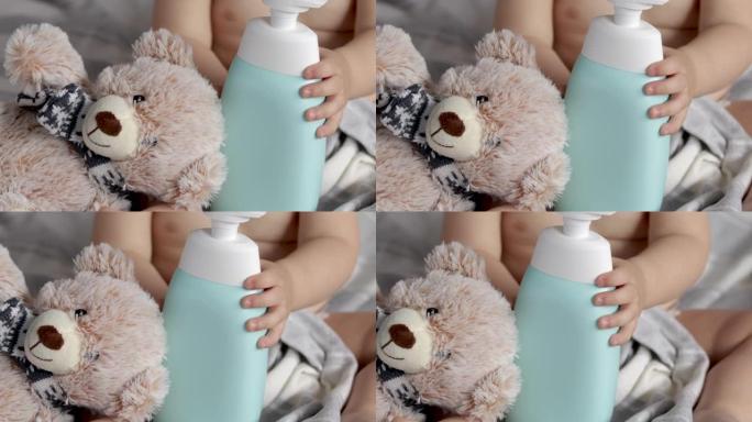 婴儿男孩孩子躺在床上，带着猫头鹰泰迪熊玩具和洗发水沐浴露瓶。蹒跚学步的婴儿肖像身体护理。学龄前儿童捡