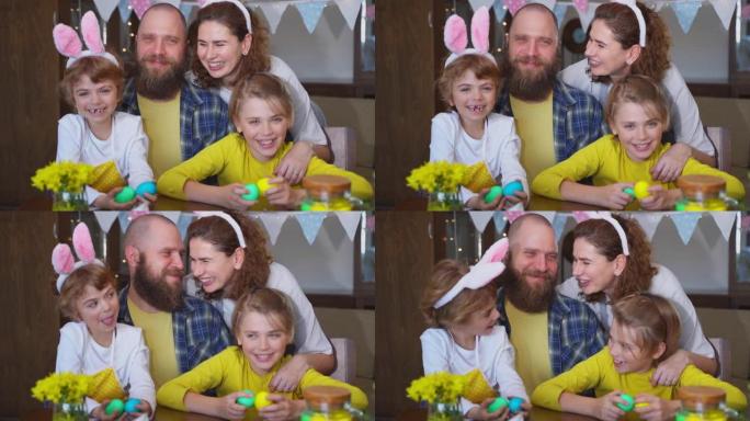 复活节周日家庭传统。父母爸爸妈妈两个白种人快乐的孩子，兔子耳朵摆姿势微笑着看着复活节装饰的鸡蛋的相机