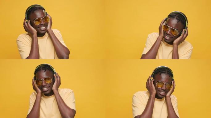戴着耳机跳舞的黑人非裔美国人快乐地听着音乐，手中的智能手机在黄色背景上摆动手臂上下微笑的太阳镜。积极